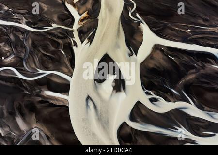Accattivante ripresa aerea che cattura gli intricati motivi e i colori contrastanti di un bacino fluviale islandese che serpeggia attraverso il terreno vulcanico scuro Foto Stock