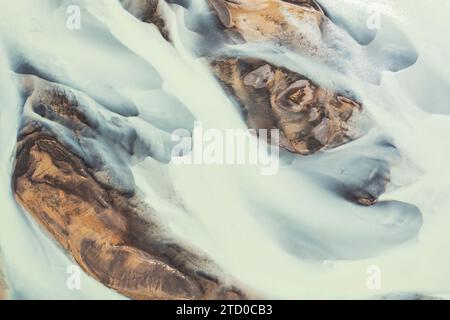 La foto aerea cattura la bellezza eterea dei bacini fluviali dell'Islanda, drappeggiati di neve e incorniciati da toni terrosi Foto Stock
