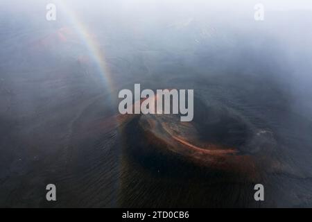 Una vista aerea cattura un debole arco arcobaleno sopra il nebbioso bacino fluviale negli aspri paesaggi dell'Islanda Foto Stock