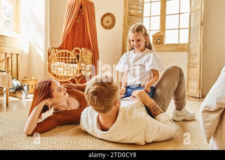 donna sorridente che guarda il marito che gioca con la figlia sul pavimento in salotto, legando momenti Foto Stock