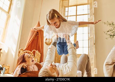 una donna che ride che guarda il marito che gioca con la figlia sul pavimento in salotto, legando momenti Foto Stock