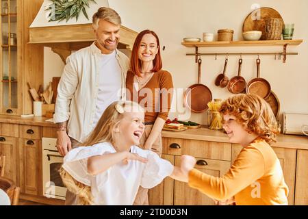 genitori felici che guardano i bambini spensierati che giocano e si divertono in cucina, con i fratelli e sorelle Foto Stock