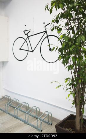 Arte della bicicletta nera su una parete bianca sopra la griglia di una pianta fresca in vaso in un ufficio creativo e moderno Foto Stock