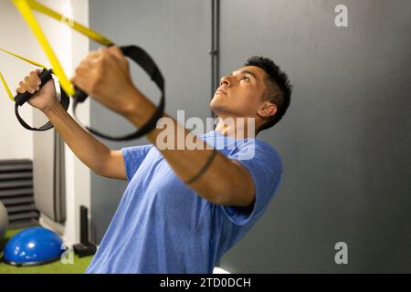 Un uomo concentrato che esegue esercizi di sospensione con bande TRX in una moderna palestra, dimostrando forza e forma fisica. Foto Stock