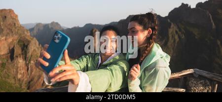 Giovane donna allegra che scatta selfie con un'amica tramite smartphone in cima alla montagna durante il weekend Foto Stock