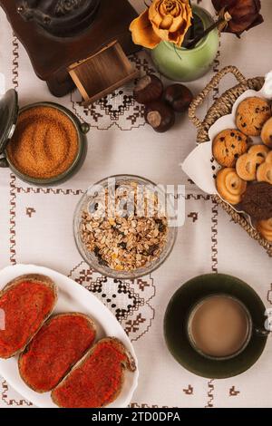 Colazione intima con pasticcini, muesli, caffè e tostini di pomodoro su una tovaglia a motivi geometrici. Foto Stock