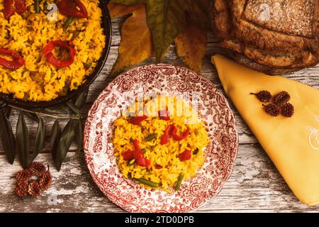 Piatto di riso colorato guarnito con verdure, accompagnato da un pezzetto di formaggio e fette di pane rustico, presentato su un tavolo di legno. Foto Stock