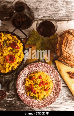 Un ambiente rustico autunnale con paella, pane artigianale e un bicchiere di vino rosso, con piatti caldi e confortevoli, perfetti per la stagione. Foto Stock