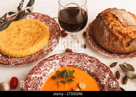 Un'elegante cena con omelette spagnole e salmorejo con crostini, pane croccante fresco e un bicchiere di vino rosso. Foto Stock