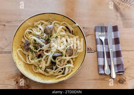 Vista dall'alto della deliziosa fettuccine appena cucinata con vongole servita in piatto con posate e tovagliolo su un tavolo di legno al ristorante Foto Stock