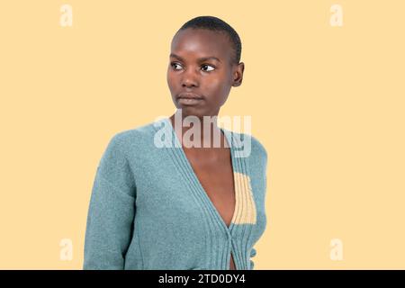 Ritratto di una giovane donna afroamericana in maglione blu con capelli neri corti che guardano lontano su sfondo giallo Foto Stock