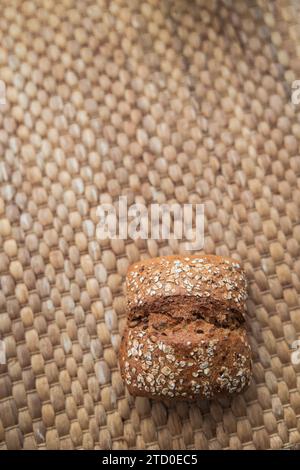 Una pagnotta di pane integrale appena sfornata con semi, appoggiata su un tappeto intrecciato testurizzato, che esemplifica la semplicità rustica Foto Stock