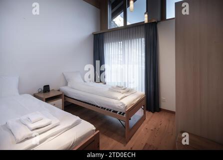 Una camera d'hotel pulita e moderna con due letti singoli ordinati, arredamento minimalista e luce naturale soffusa. Foto Stock