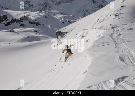 Alto angolo di anonimo sciatore maschile che salta dalla maestosa pista innevata di montagna nella soleggiata giornata di Zermatt, Svizzera Foto Stock