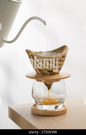 Versare l'acqua calda sul caffè macinato in un gocciolatoio fatto di tessuto di bambù. Foto Stock