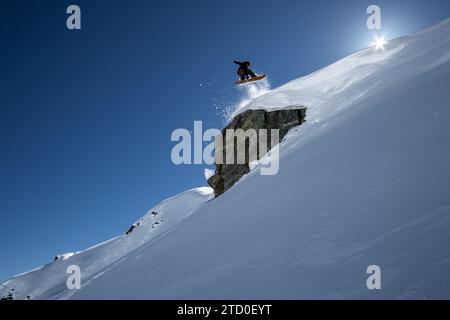 Dal basso, potrai ammirare lo snowboarder senza paura che salta sopra la formazione rocciosa su un paesaggio innevato durante le vacanze invernali in Canada Foto Stock