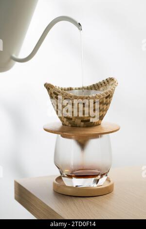 Versare l'acqua calda sul caffè macinato in un gocciolatoio fatto di tessuto di bambù. Foto Stock