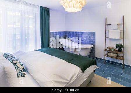 Camera da letto elegante e moderna con bagno aperto con vasca indipendente e scaffalature eleganti. Foto Stock