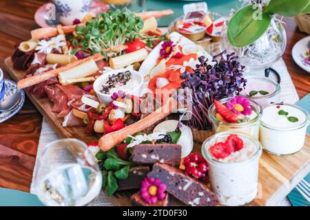 Una vivace tavola di salumi gourmet piena di un assortimento di formaggi, carni e fiori commestibili. Foto Stock