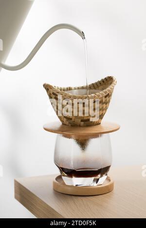 Versare l'acqua calda sul caffè macinato in un gocciolatoio fatto di tessuto di bambù. Foto Stock