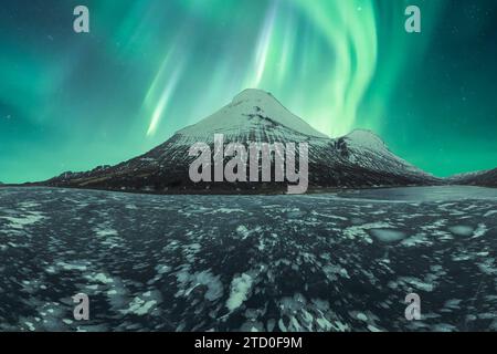 L'affascinante aurora boreale balla su una montagna innevata nel tranquillo paesaggio islandese. Foto Stock