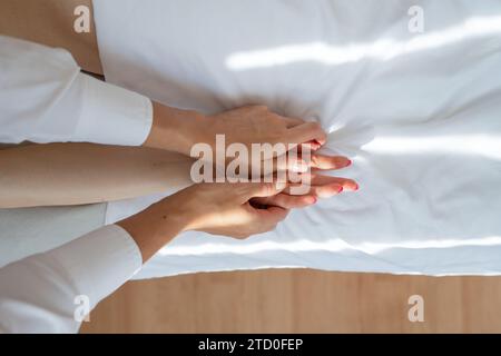 Terapista anonimo ad alto angolo che esegue un massaggio di agopuntura sulla mano del cliente femminile su un comodo letto bianco nel salone della spa durante la sessione Foto Stock