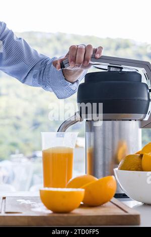 Anonimo cuoco maschio raccolto in piedi al tavolo della cucina con spremiagrumi e tagliati a metà arancia fresca in ciotola durante un sano processo di colazione durante il giorno Foto Stock