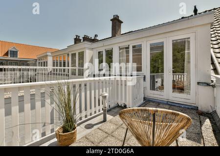 Sedia in vimini a pianta sul balcone, oltre a porta di vetro chiusa e finestre dell'appartamento nelle giornate di sole Foto Stock