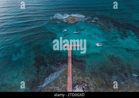 Una tranquilla vista aerea di un molo di legno che si estende nelle vivaci acque blu di una barriera corallina al largo della costa di Cancun Foto Stock