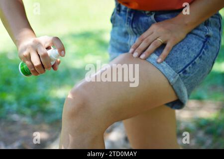 Primo piano di una giovane donna che applica repellente per insetti sulla gamba nel parco Foto Stock