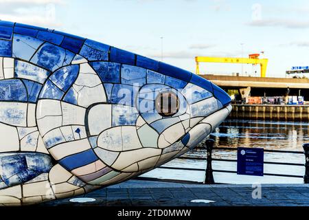 Scultura Salmon of Knowledge o Big Fish, con due gru gialle a cavalletto Samson e Golia lungo il fiume Lagan, Belfast, Irlanda del Nord. Foto Stock