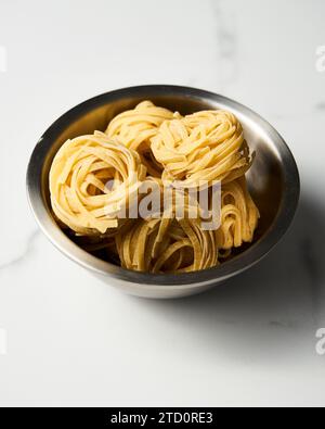 Tagliolini secchi o tagliatelle in nidi nel recipiente su fondo bianco. Ingrediente crudo Foto Stock