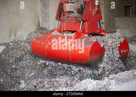 Una gru a ponte rossa si afferra durante la movimentazione del combustibile derivato dai rifiuti. Trattamento dei rifiuti solidi urbani in una fonte di energia. Foto Stock