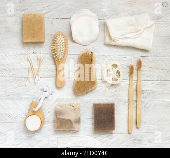 Saponette e articoli per l'igiene naturale vista dall'alto su un tavolo in legno bianco. Asciugamano, spugne e spazzolino naturali, spazzolini da denti in bambù e tamponi di cotone, vista dall'alto Foto Stock