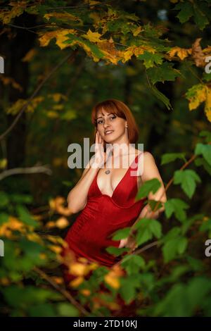 Una donna sorridente a testa rossa si pone con grazia nel caldo bagliore di un tramonto autunnale. Perfetto per catturare la magia dell'autunno e la bellezza della stagione. Foto Stock