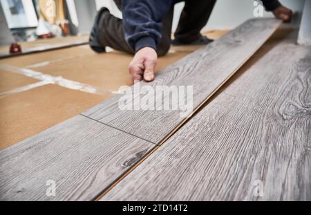 Primo piano di un operaio edile che installa pavimenti in legno laminato nell'appartamento in ristrutturazione. Mani maschili che posizionano tavole laminate sul pavimento a casa. Concetto di rinnovo del pavimento. Foto Stock