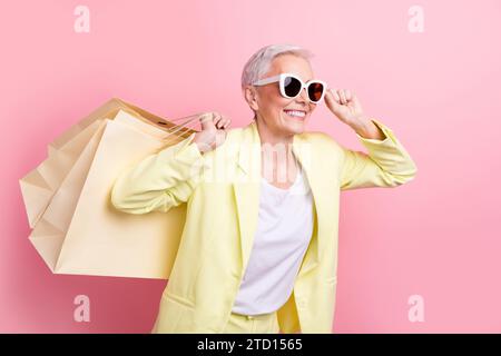 Foto di fantastici pacchetti da donna d'affari che guardano gli occhiali da sole alla ricerca di occasioni in un centro commerciale isolato su sfondo rosa Foto Stock