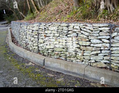 Il bordo della carreggiata con un muro di contenimento gabion Foto Stock