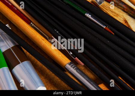 vecchie tele con un set di pennelli da pittura e alcuni tubi di vernici ad olio giacciono su un tavolo di legno Foto Stock