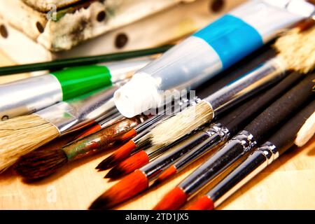 vecchie tele con un set di pennelli da pittura e alcuni tubi di vernici ad olio giacciono su un tavolo di legno Foto Stock