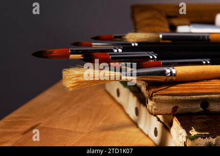 vecchie tele con un set di pennelli da pittura e alcuni tubi di vernici ad olio giacciono su un tavolo di legno Foto Stock