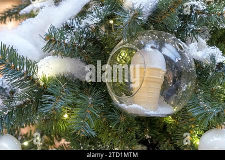 Gelato in una tazza per waffle all'interno di una palla trasparente sull'albero di Natale. Concetto di nuovo anno. Foto Stock