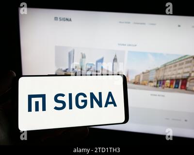 Persona che possiede uno smartphone con il logo della società immobiliare austriaca Signa Holding GmbH davanti al sito web. Concentrarsi sul display del telefono. Foto Stock