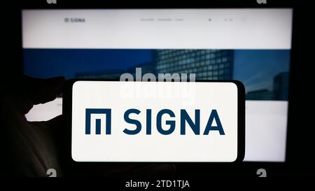 Persona in possesso di un cellulare con il logo della società immobiliare austriaca Signa Holding GmbH davanti alla pagina web aziendale. Concentrarsi sul display del telefono. Foto Stock