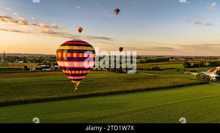 Una vista aerea di quattro mongolfiere che galleggiano sulle fattorie rurali di campi di mais e Alfalfa in una soleggiata giornata estiva Foto Stock