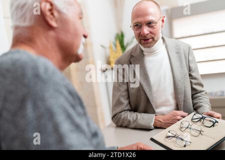 Ottico che mostra gli occhiali da vista a un uomo anziano. Sta scegliendo gli occhiali nel negozio di ottica. Foto Stock