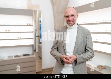 un'ottica sorridente con gli occhiali in un negozio. Ha le mani strette e si trova in un negozio di occhiali. Foto Stock