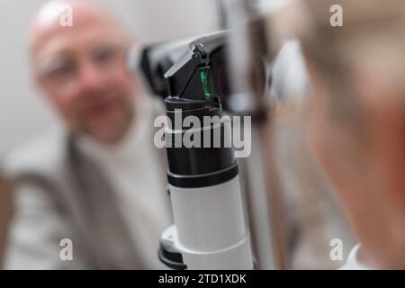 L'apparecchiatura di optometria ha una lampada a incandescenza con il paziente e l'optometrista sfocati sullo sfondo Foto Stock