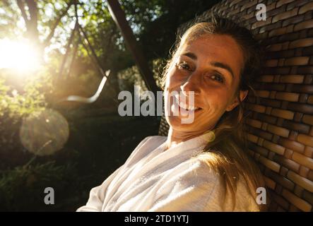 Donna sorridente su un'altalena da giardino, sole che splende tra gli alberi Foto Stock