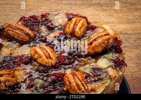 torta al rum con noci pecan, ananas, ciliegie secche e mirtilli rossi contro legno rustico Foto Stock